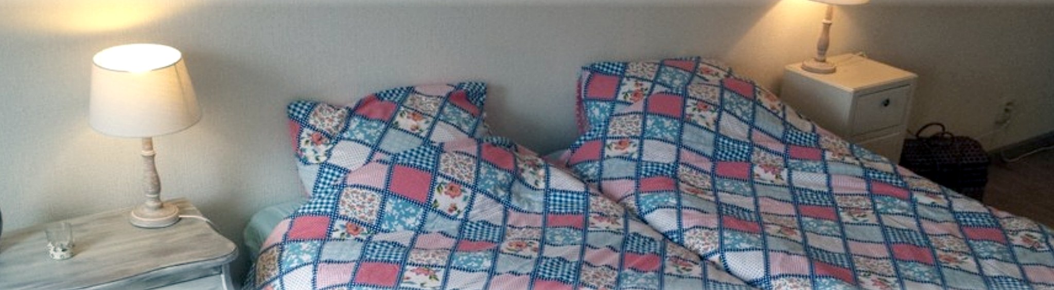 Een opgemaakt bed met een patchwork sprei en twee schemerlampen in de Bêd en Brochje