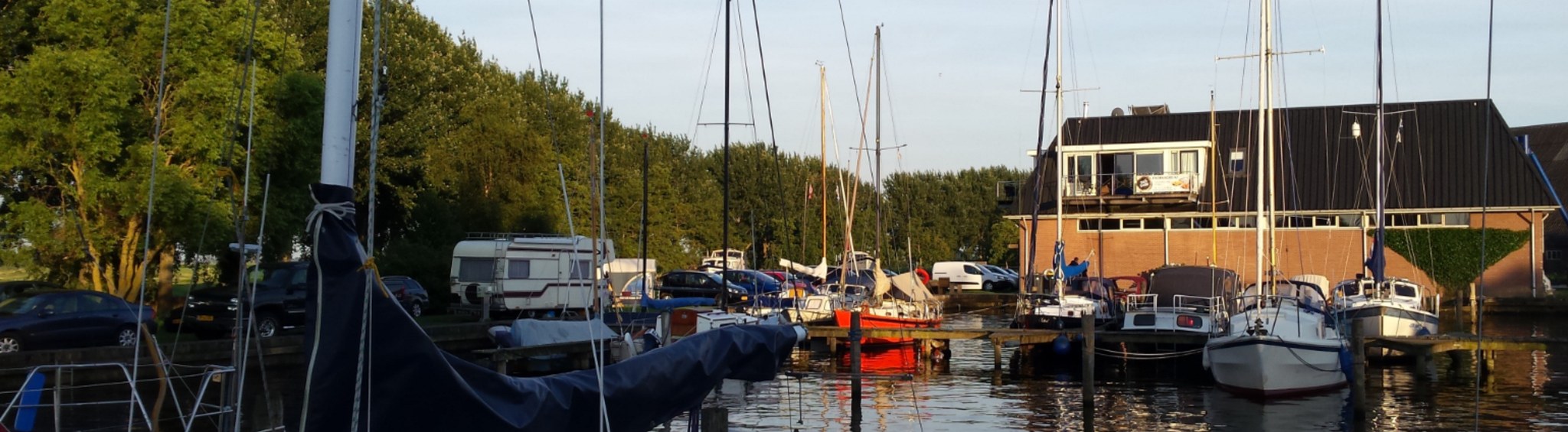 De haven in de avondzon, met masten, afgemeerde boten en het havengebouw met balkon