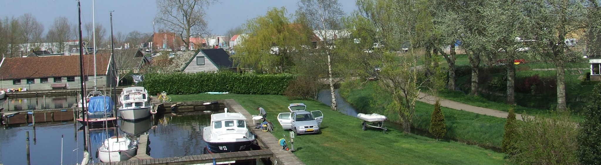 De haven in het voorjaar, met het gazon langs het water en een bijboot op een trailer