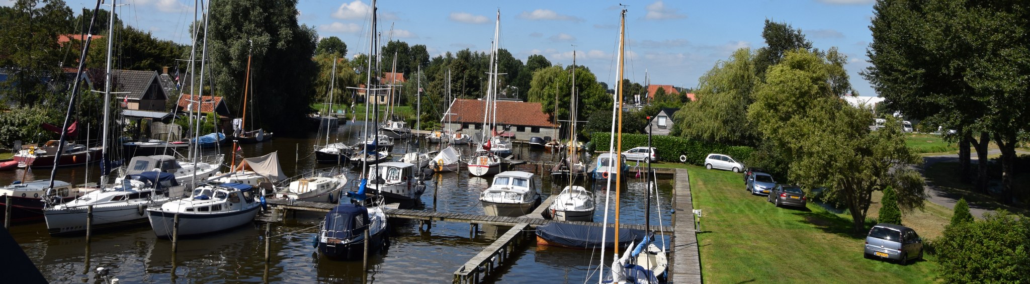 De haven van Yachtservice It Ges op een zomerse dag, met de steigers, de afgemeerde boten en het gazon langs de kade