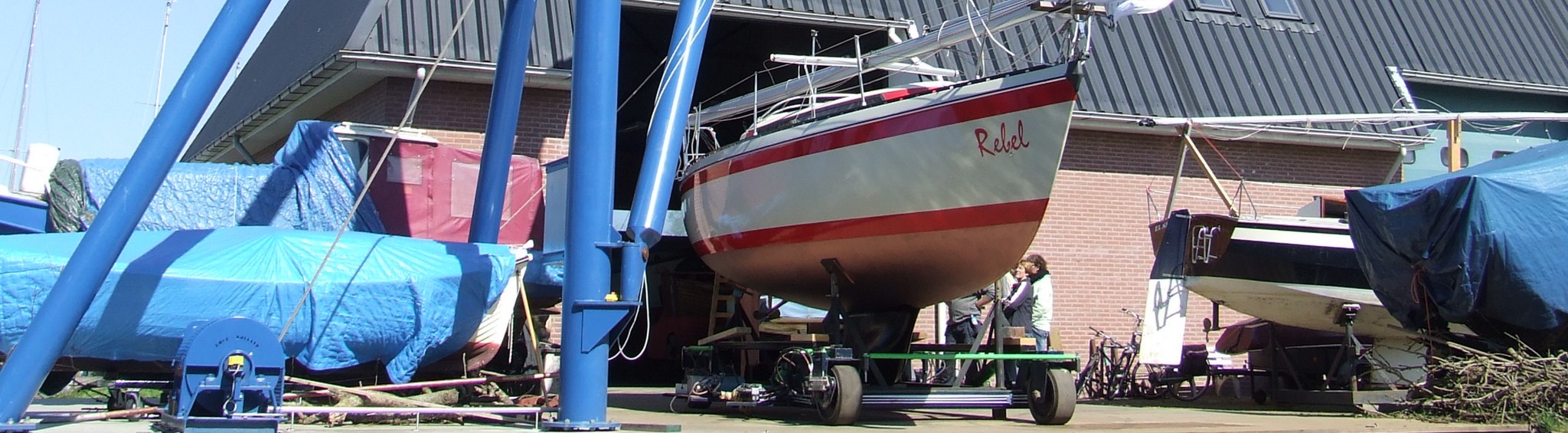 De blauwe kraan van de haven houdt een zeiljacht vrij van de grond, met de Crawler eronder klaar om het schip weg te rijden